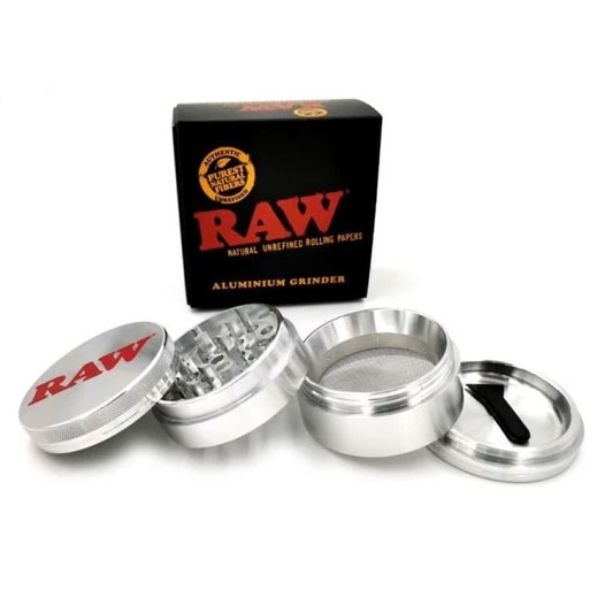An aluminium herb grinder shown open with its four pieces arranged in front, alongside its black RAW brand box on a white background.